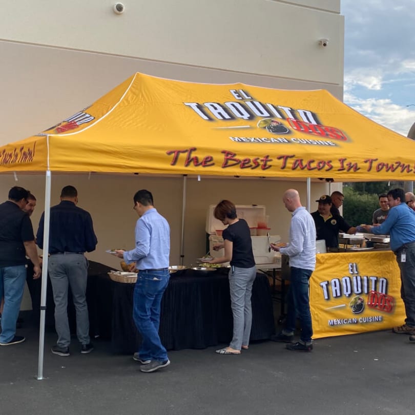 People serving themselves Mexican food from El Taquito Restaurant Dos under a yellow tent.