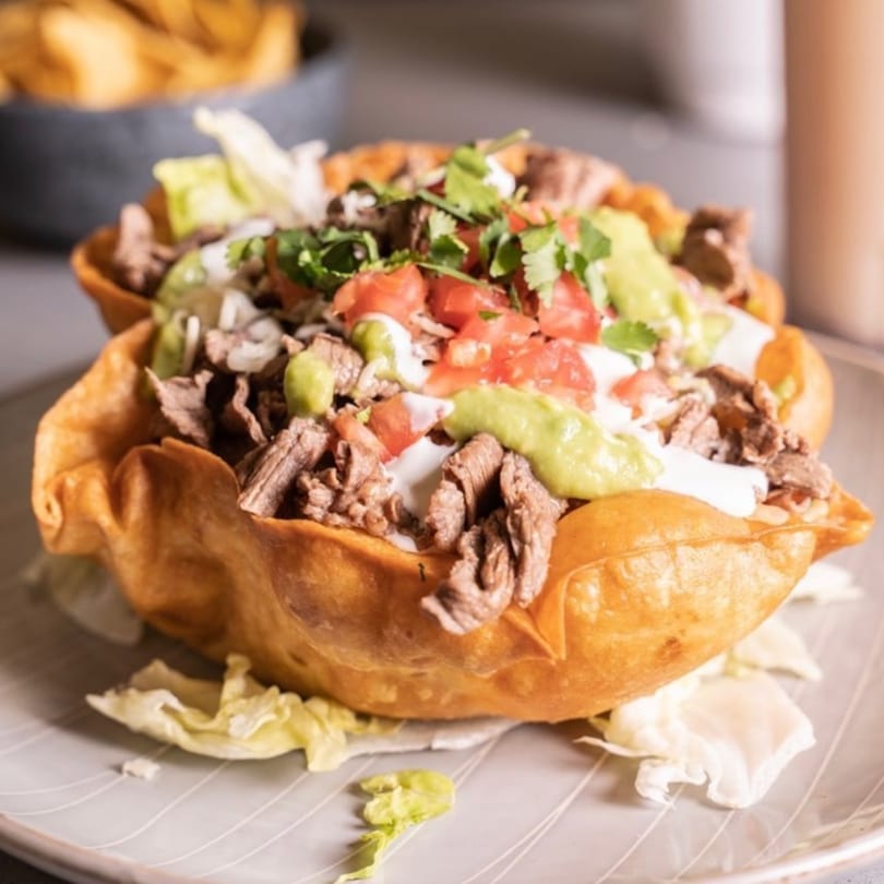 A crispy taco salad bowl from El Taquito Restaurant Dos, filled with steak, lettuce, tomatoes, and guacamole.
