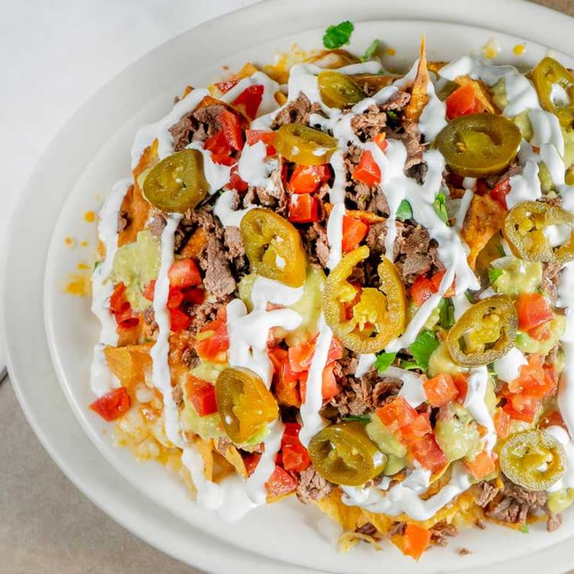 A close-up of El Taquito Restaurant Dos's nachos, topped with meat, tomatoes, jalapeños, and sour cream.