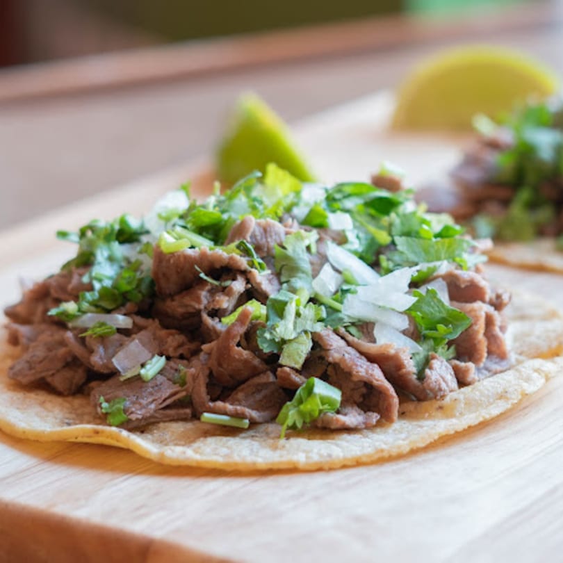 Close-up of a Mexican street taco with carne asada, cilantro, and diced onions on a wooden surface.