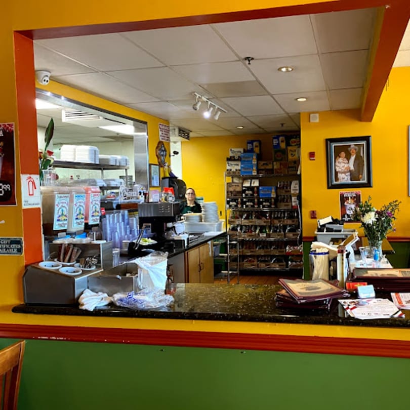A vibrant yellow and green Mexican restaurant interior with a counter, drink dispensers, and a person behind the bar.
